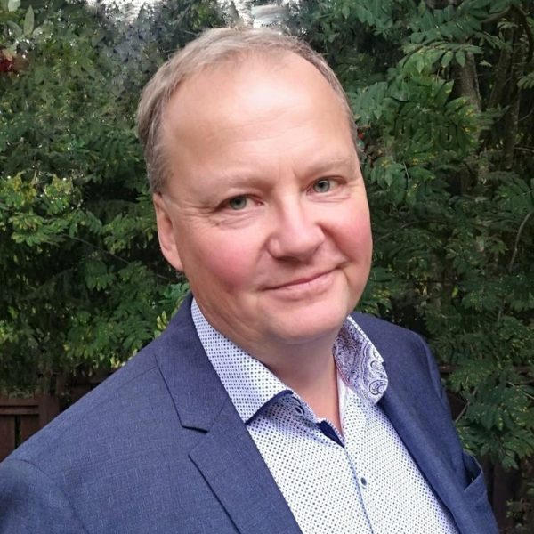 Mies puku päällä katsoo suoraan kameraan ja hymyilee.