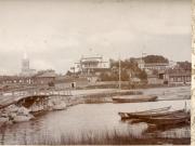 Kuvan etualan Pitkäsilta ja Baltzaborgin talot johdattavat katseen Vallimäelle ja edelleen kirkontorneihin, jotka piirtävät horisonttiin kaupungin tunnistettavan siluetin. Vallimäellä ravintola, puinen pitkän mallinen keilaratarakennus sekä luotsiasema Kaupunkikuva, kuvattu Kainpirtin suunnasta kohti kaupunkia. Etualalla ns. Pitkäsilta, Baltzarborgin asuinaluetta, sitten Vallimäki, jossa ravintola Vallila, puinen keilaratararakennus ja luotsiasema. Uuden ja vanhan kirkon tornit näkyvissä. Veneitä rannassa.