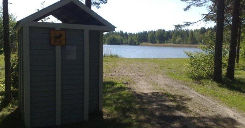 Pukukoppi sekä polku uimarannalle, taustalla näkyy järvi