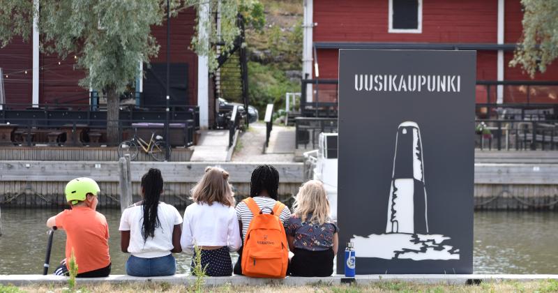 Lapset istuvat uudenkaupungin kaupunginlahden rannalla selkä kameraan päin. 