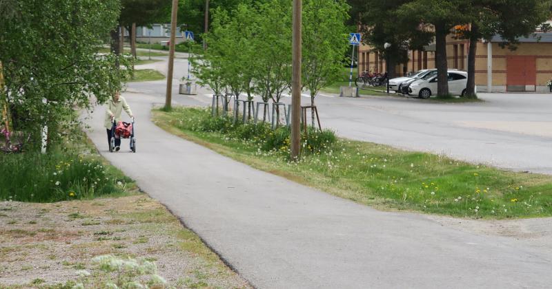 Kuvassa katualuetta Kalannista. Taustalla vanhus rollaattorin kanssa ja autoja parkissa. Pyörätie sekä ajoväylä.