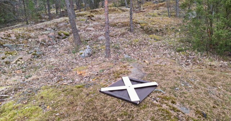 Valkoinen X-mallinen signaalimerkki alkukevään harmahtavassa maastossa.