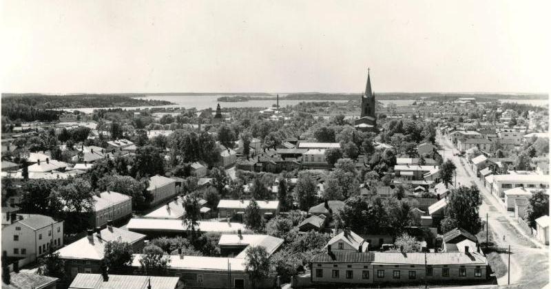 sisällön kuvaus: Valokuvapostikortti. Yleisnäkymä kaupungista, Myllymäen vesitornista kuvattuna. Etualalla Myllykatu, oikealla Vuorikatu, vasemmalla Ylinenkatu ja museo. Taustalla uusi ja vanha kirkko. Kaupunkikuva