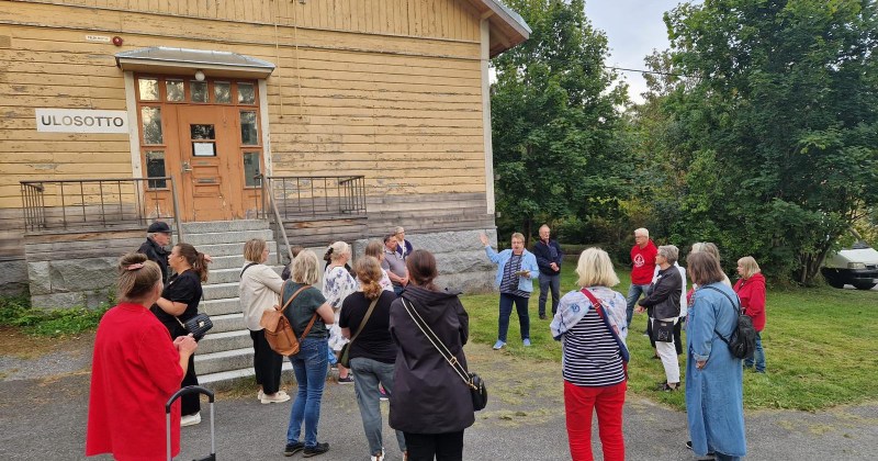 ihmisiä ulkona kuuntelemassa opasta.