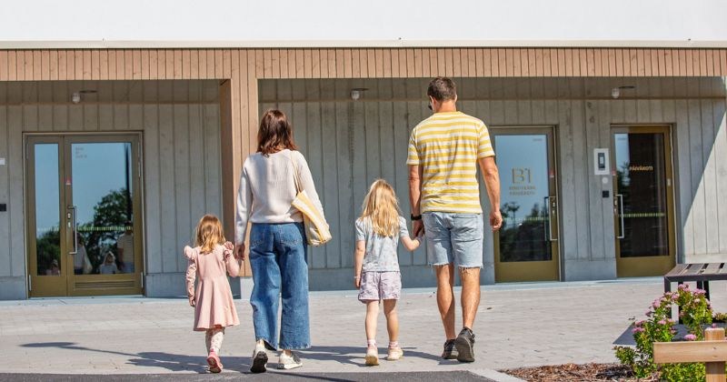 Kaksi lasta ja kaksi aikuista kävelee käsi kädessä kohti päiväkotia.