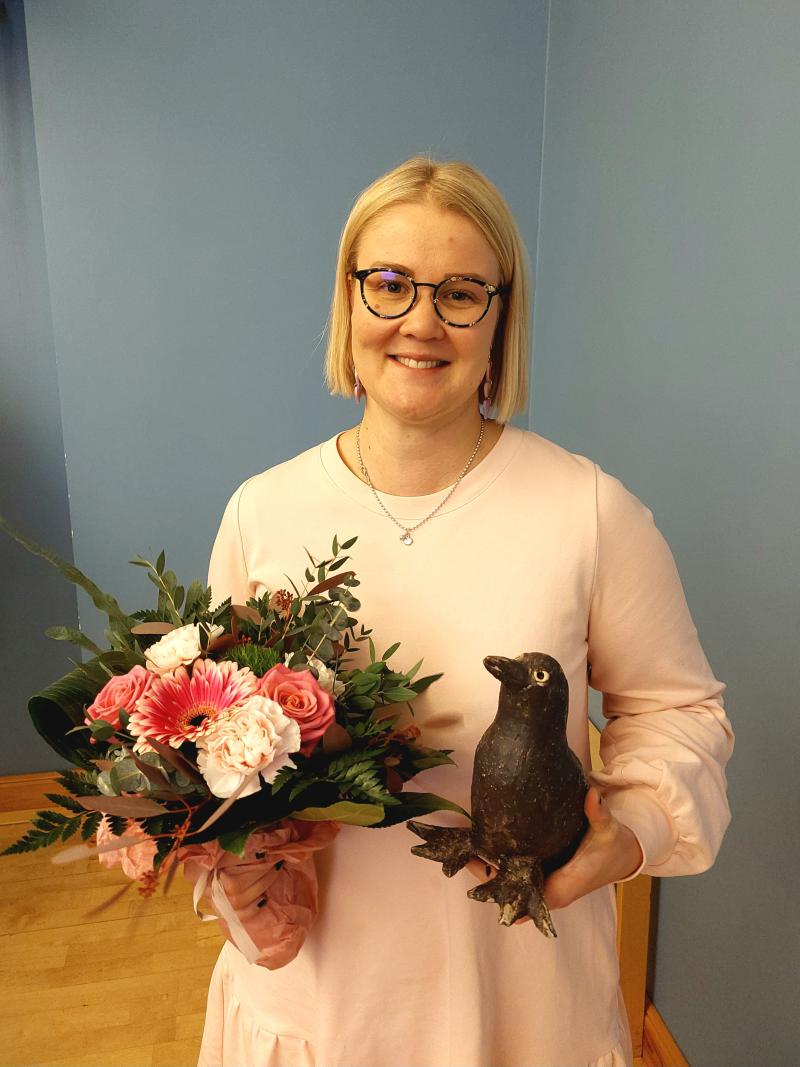Naakka patsaan saajana vaalea nainen kukkien kera