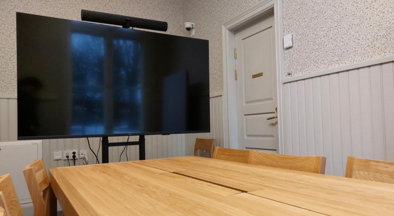 Kuva kirjaston neuvotteluhuoneen sisältä. Alareunan peittää neuvottelupöytä. Musta televisioruutu sijaitsee vasemmalla.